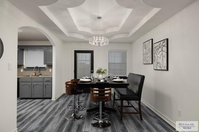 dining space featuring dark wood-style floors, a tray ceiling, arched walkways, an inviting chandelier, and baseboards