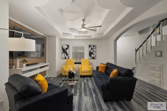 living area with arched walkways, a ceiling fan, baseboards, stairs, and a tray ceiling