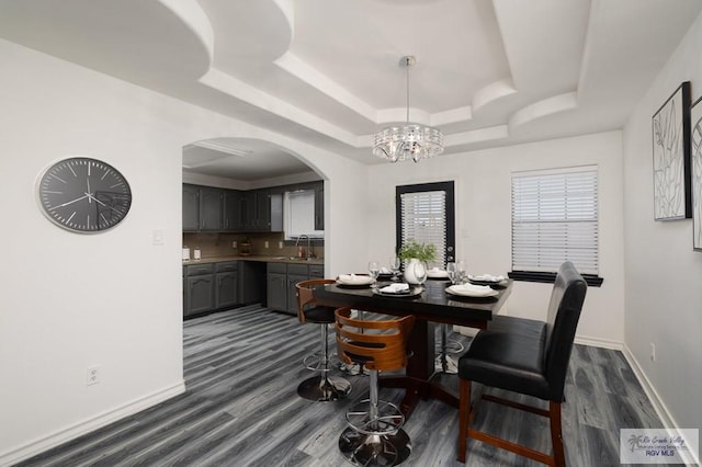 dining area with arched walkways, a tray ceiling, dark wood-type flooring, and baseboards