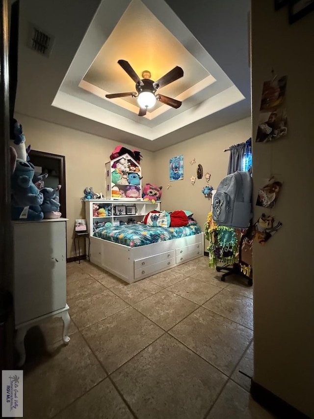 bedroom with a tray ceiling, visible vents, and ceiling fan