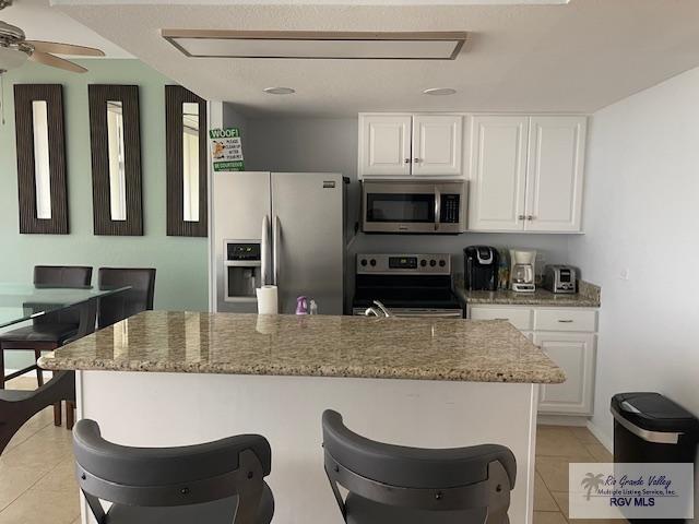 1000 Padre Blvd Unit 307, South Padre Island, TX 78597 - kitchen with appliances with stainless steel finishes, light tile patterned floors, white cabinetry, and a breakfast bar area