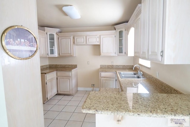487 Agua Viva Ln, Brownsville, TX 78521 - kitchen featuring a sink, glass insert cabinets, light tile patterned floors, light stone countertops, and a peninsula