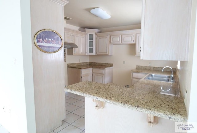 487 Agua Viva Ln, Brownsville, TX 78521 - kitchen with a sink, a peninsula, a kitchen breakfast bar, light stone countertops, and light tile patterned floors