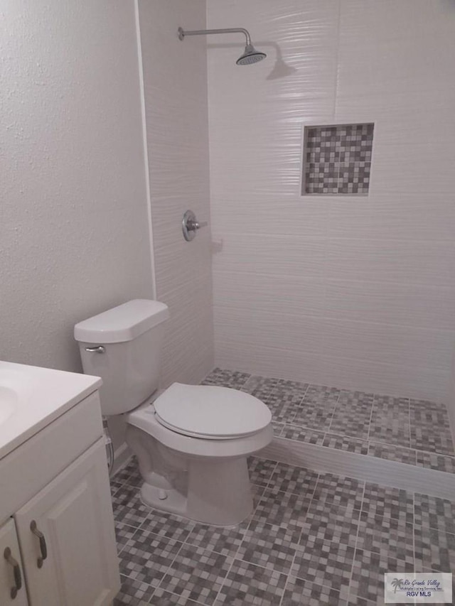 full bathroom featuring toilet, a tile shower, and vanity