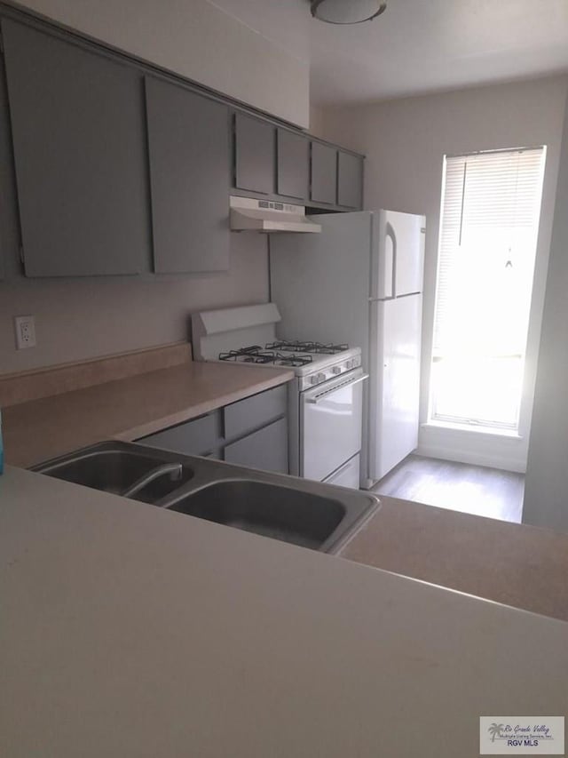 kitchen with gray cabinets, a sink, white range with gas stovetop, and under cabinet range hood