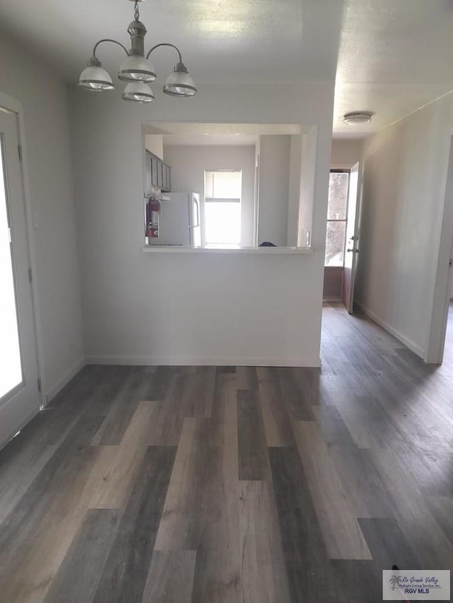 unfurnished dining area featuring a chandelier, plenty of natural light, baseboards, and wood finished floors