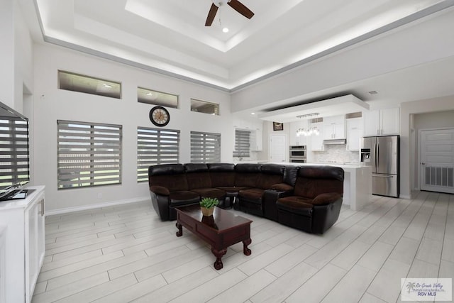 living room with a tray ceiling, ceiling fan, and a towering ceiling