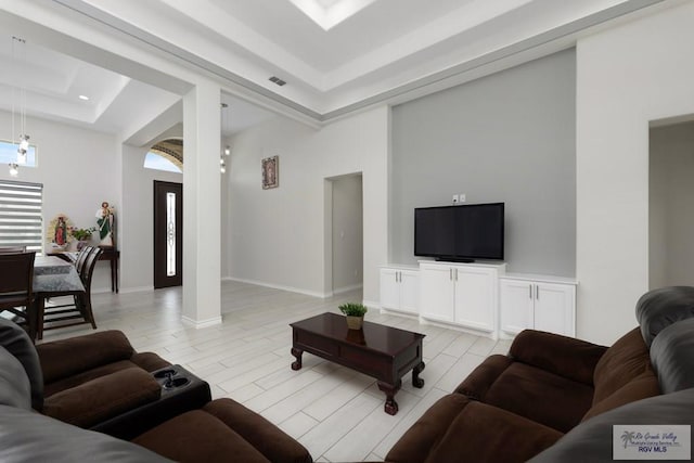 living room featuring a towering ceiling, a tray ceiling, and light hardwood / wood-style flooring