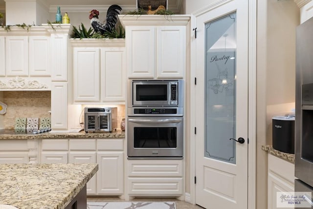 kitchen featuring white cabinets, light stone countertops, ornamental molding, appliances with stainless steel finishes, and tasteful backsplash