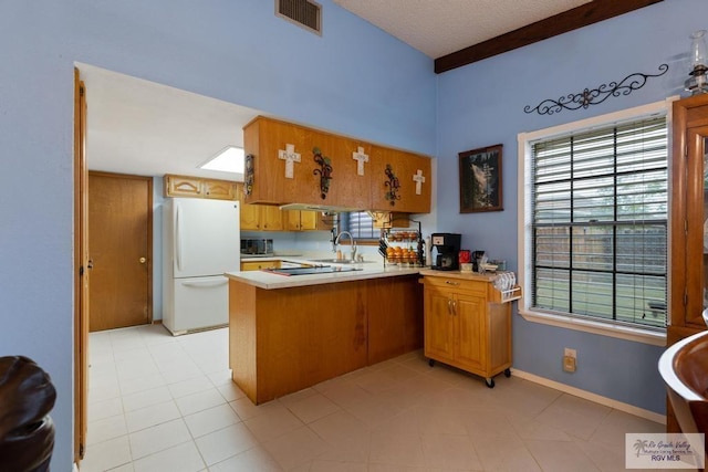 kitchen featuring white fridge, light tile patterned floors, kitchen peninsula, beamed ceiling, and sink