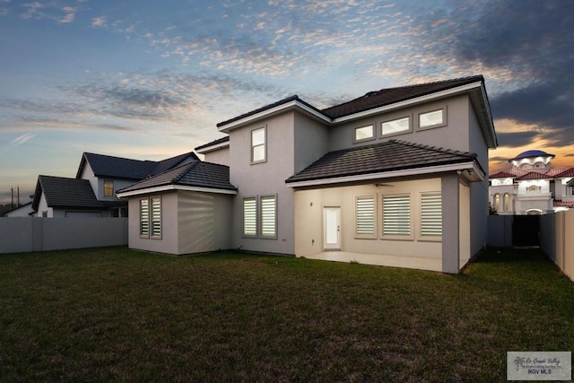 back house at dusk featuring a lawn and ceiling fan