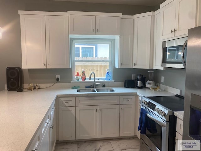 kitchen with stainless steel appliances, light countertops, marble finish floor, a sink, and white cabinetry