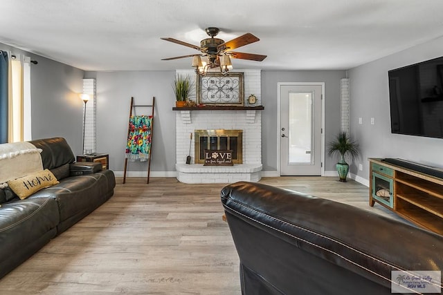 living room featuring a ceiling fan, a brick fireplace, baseboards, and wood finished floors