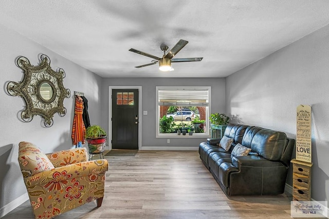 living area featuring wood finished floors, a ceiling fan, and baseboards