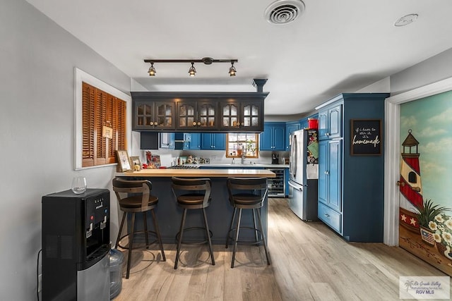 bar with visible vents, wine cooler, freestanding refrigerator, light wood-type flooring, and a sink