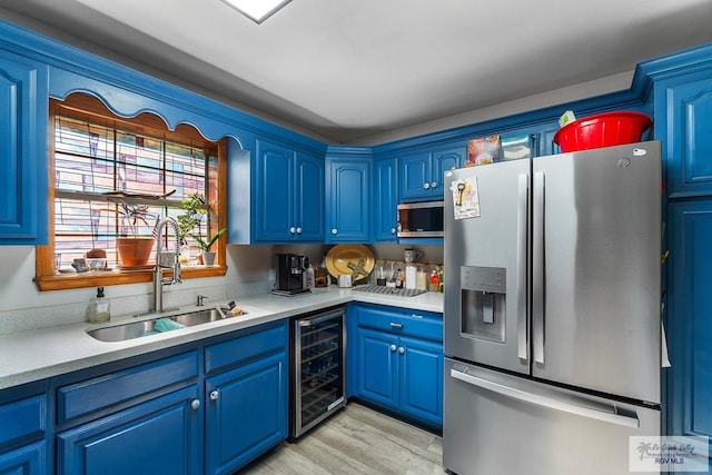 kitchen with wine cooler, stainless steel appliances, light countertops, a sink, and blue cabinets