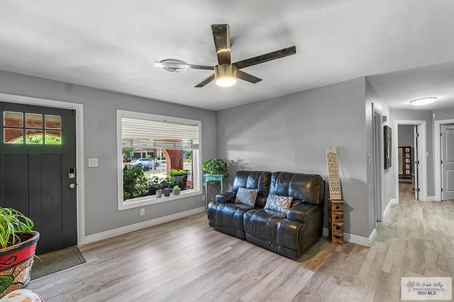 living area with a ceiling fan, light wood-style flooring, and baseboards