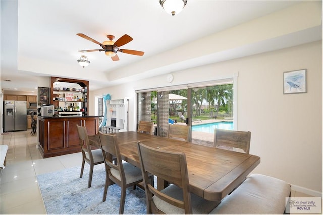 dining space with light tile patterned floors, a raised ceiling, and ceiling fan