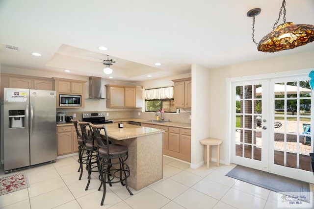 kitchen featuring french doors, wall chimney exhaust hood, a center island, a raised ceiling, and appliances with stainless steel finishes