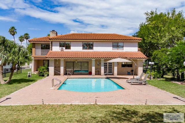 rear view of house with a balcony, a fenced in pool, a patio area, and a lawn