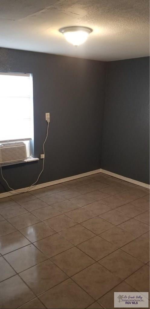 unfurnished room with cooling unit, tile patterned flooring, a textured ceiling, and baseboards