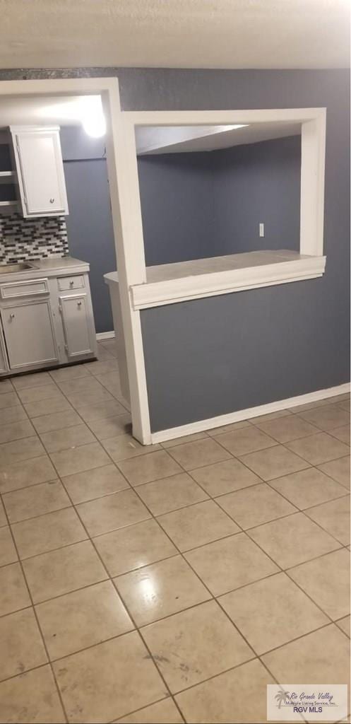 kitchen with light tile patterned flooring, baseboards, white cabinets, light countertops, and decorative backsplash