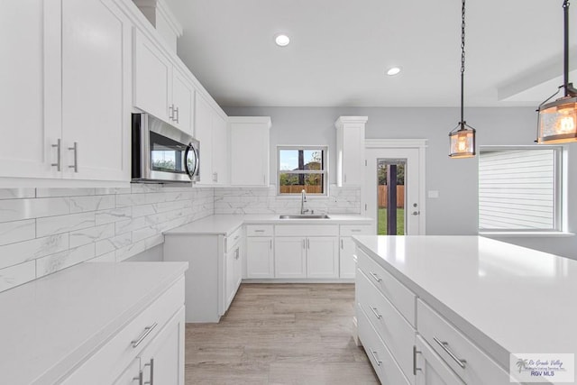 kitchen with backsplash, light hardwood / wood-style flooring, white cabinets, and hanging light fixtures