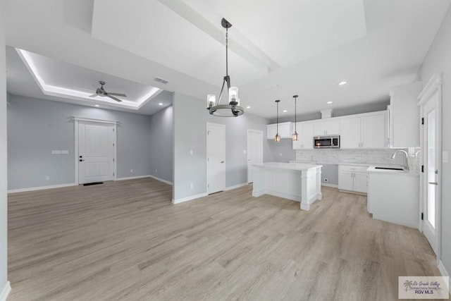 kitchen with a kitchen island, pendant lighting, light hardwood / wood-style floors, white cabinets, and ceiling fan with notable chandelier