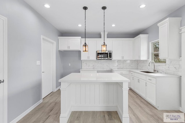 kitchen with white cabinets, decorative light fixtures, a kitchen island, and sink