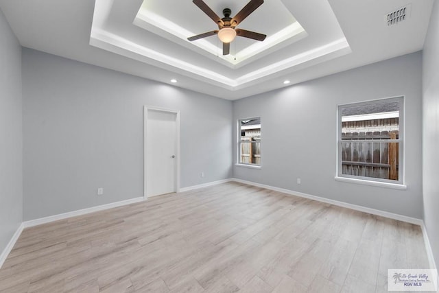 empty room with ceiling fan, light hardwood / wood-style floors, and a tray ceiling