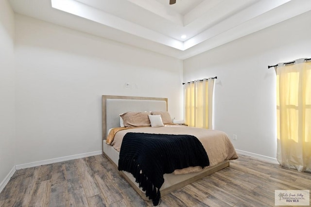 bedroom featuring wood-type flooring, a raised ceiling, and ceiling fan