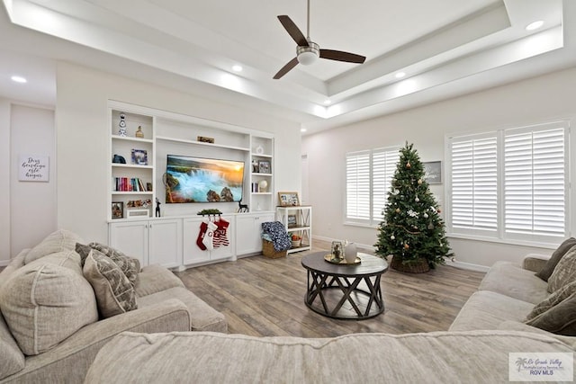 living room with a tray ceiling, light hardwood / wood-style flooring, and ceiling fan