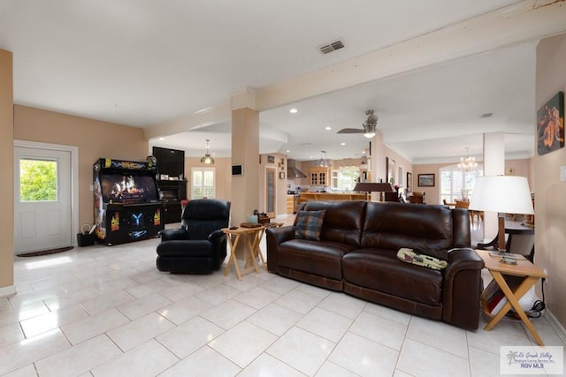 living room featuring ceiling fan with notable chandelier, a wealth of natural light, beam ceiling, and light tile patterned floors