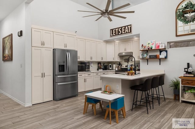 kitchen featuring appliances with stainless steel finishes, white cabinetry, a kitchen breakfast bar, kitchen peninsula, and light hardwood / wood-style flooring