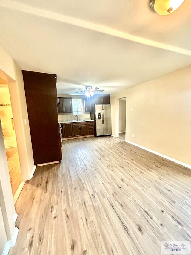 unfurnished living room with light wood finished floors, ceiling fan, baseboards, and a sink