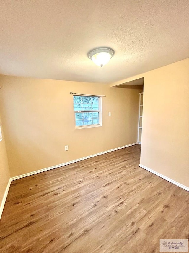 unfurnished room featuring a textured ceiling, wood finished floors, and baseboards