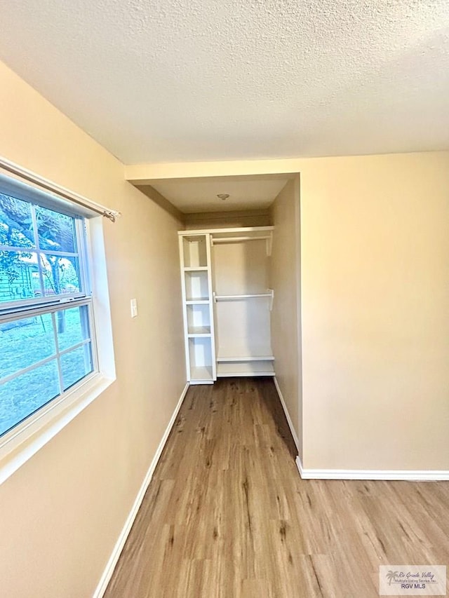 corridor with light wood-type flooring, baseboards, and a textured ceiling