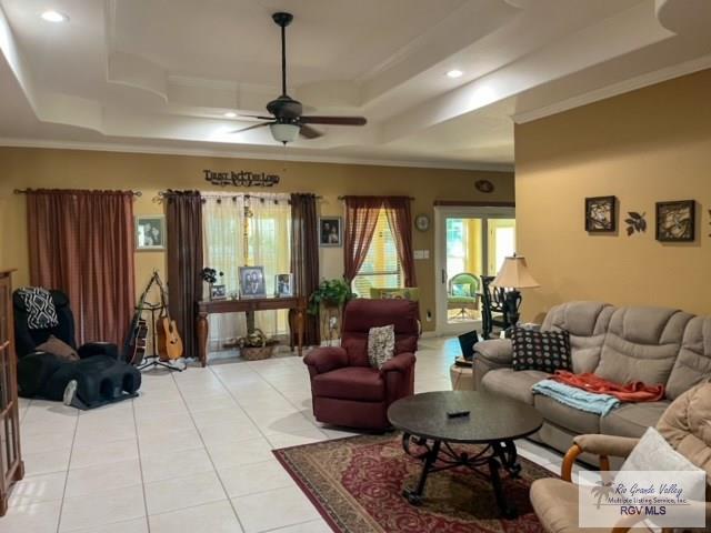 living room with ceiling fan, light tile patterned floors, ornamental molding, and a tray ceiling