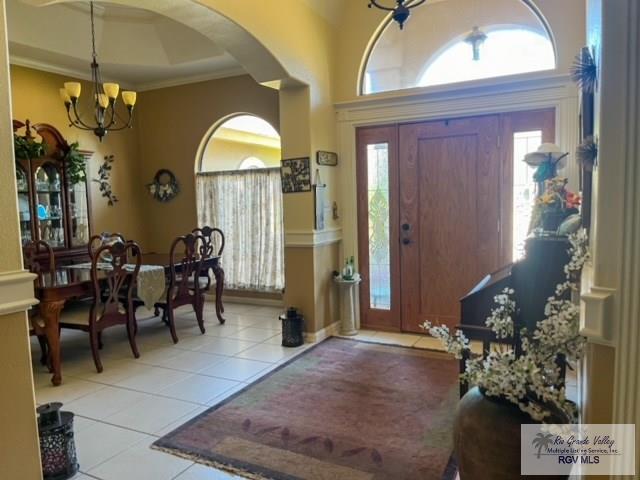 tiled entryway with crown molding, a towering ceiling, and an inviting chandelier