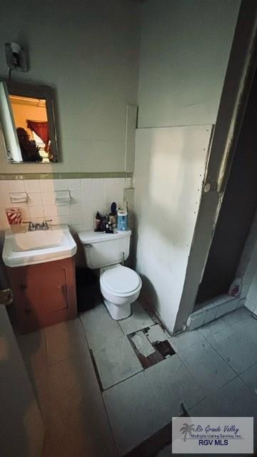 bathroom with tile patterned floors, vanity, tile walls, and toilet