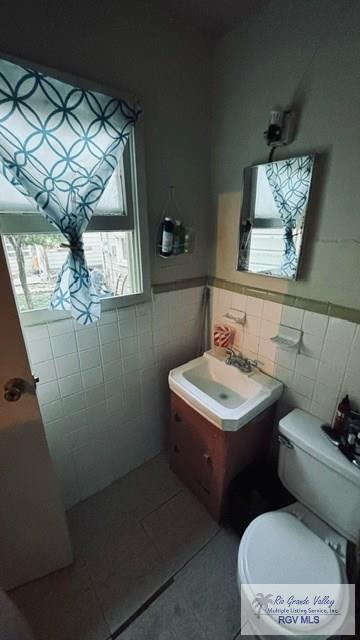 bathroom featuring tile patterned floors, vanity, tile walls, and toilet