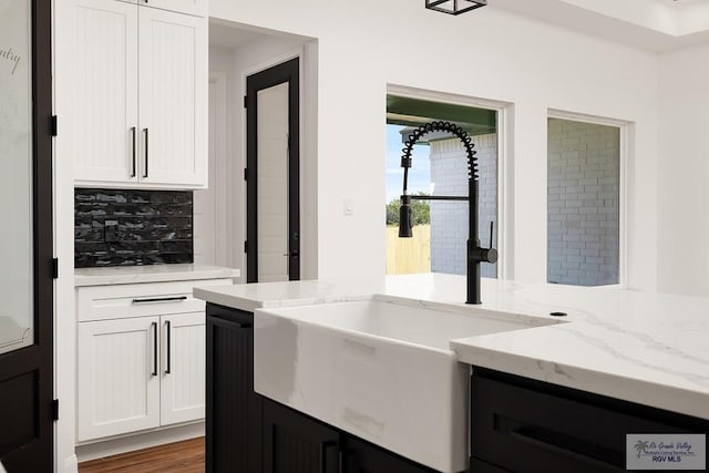 kitchen with decorative backsplash, white cabinetry, sink, and light stone counters