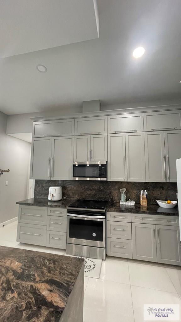 kitchen featuring recessed lighting, appliances with stainless steel finishes, gray cabinets, decorative backsplash, and dark stone countertops