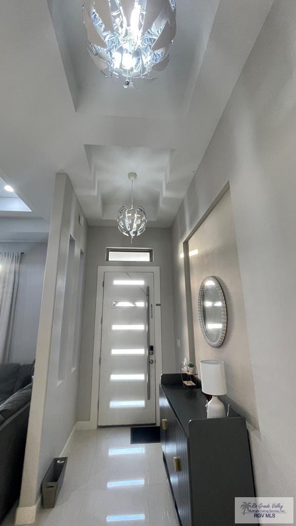 foyer entrance with light tile patterned floors, baseboards, a chandelier, and a raised ceiling