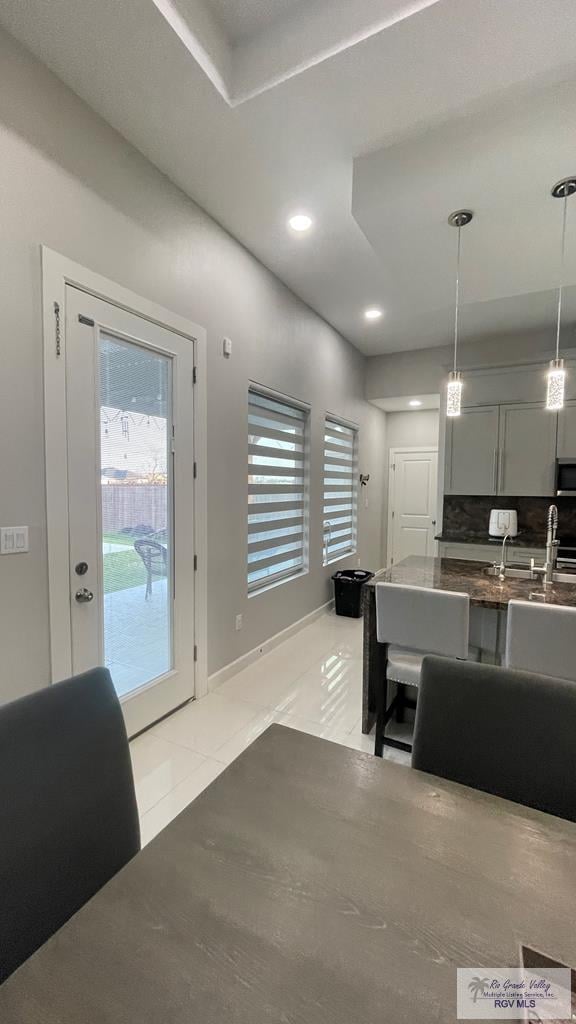 interior space featuring light tile patterned floors, dark countertops, stainless steel microwave, hanging light fixtures, and a sink