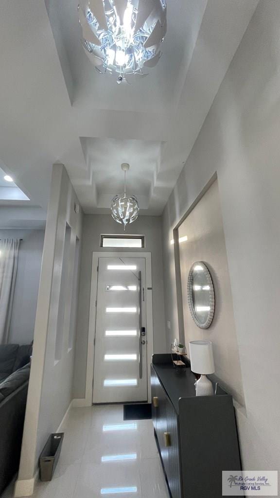 foyer entrance with a chandelier, a tray ceiling, light tile patterned flooring, and baseboards