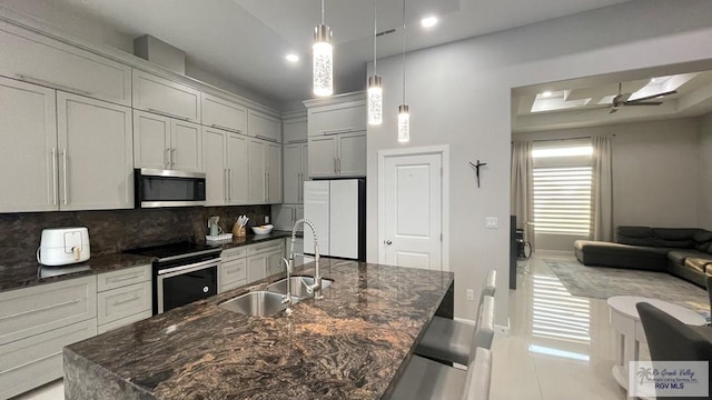 kitchen featuring a center island with sink, tasteful backsplash, appliances with stainless steel finishes, a sink, and dark stone counters