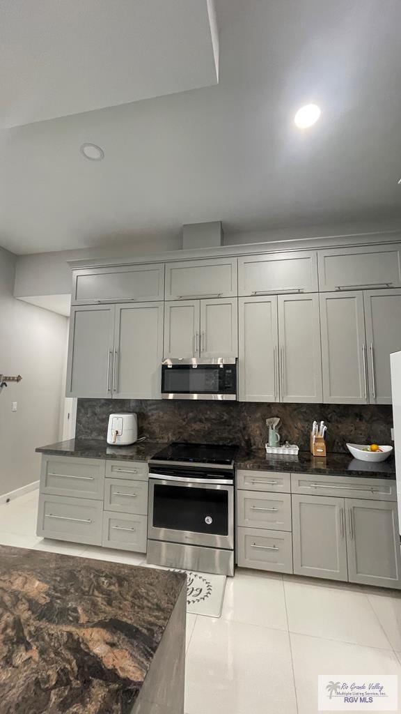 kitchen with light tile patterned floors, dark stone counters, decorative backsplash, gray cabinets, and stainless steel appliances