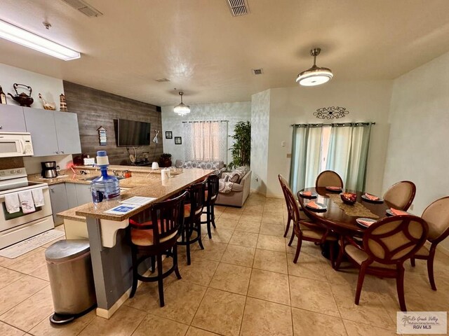 kitchen featuring pendant lighting, white appliances, light tile patterned flooring, a kitchen bar, and kitchen peninsula