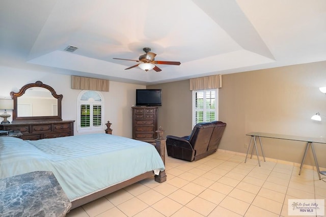 tiled bedroom with ceiling fan, a raised ceiling, and multiple windows